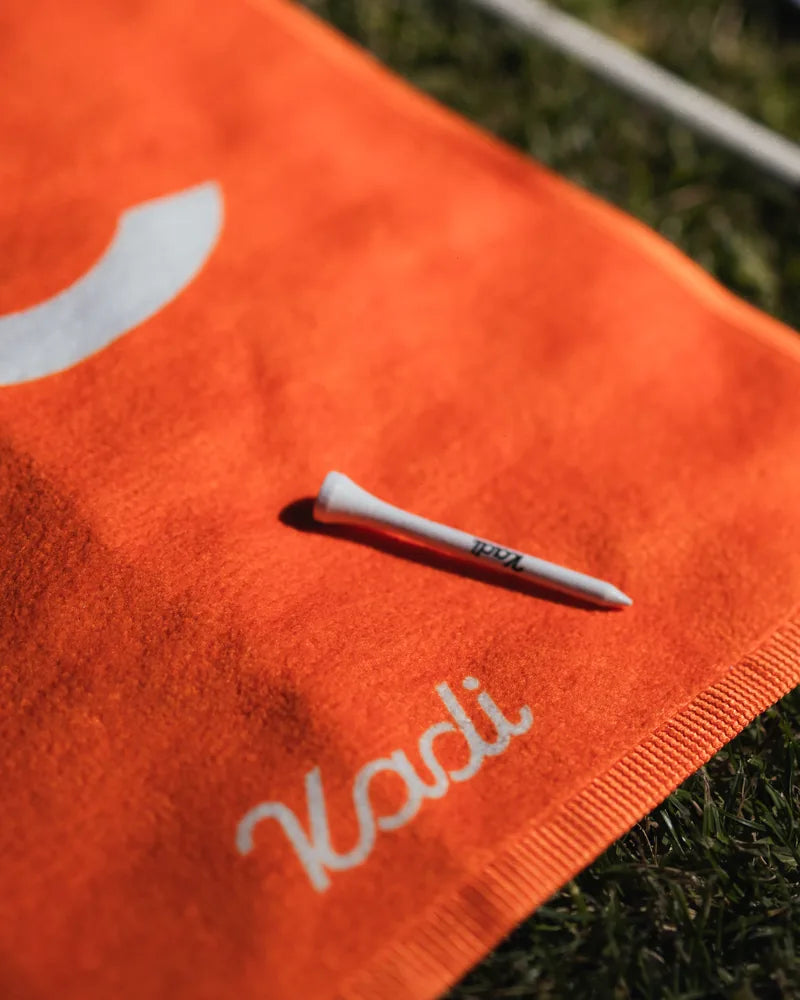 Close-up of an orange KADI golf towel with a tee on the grass
