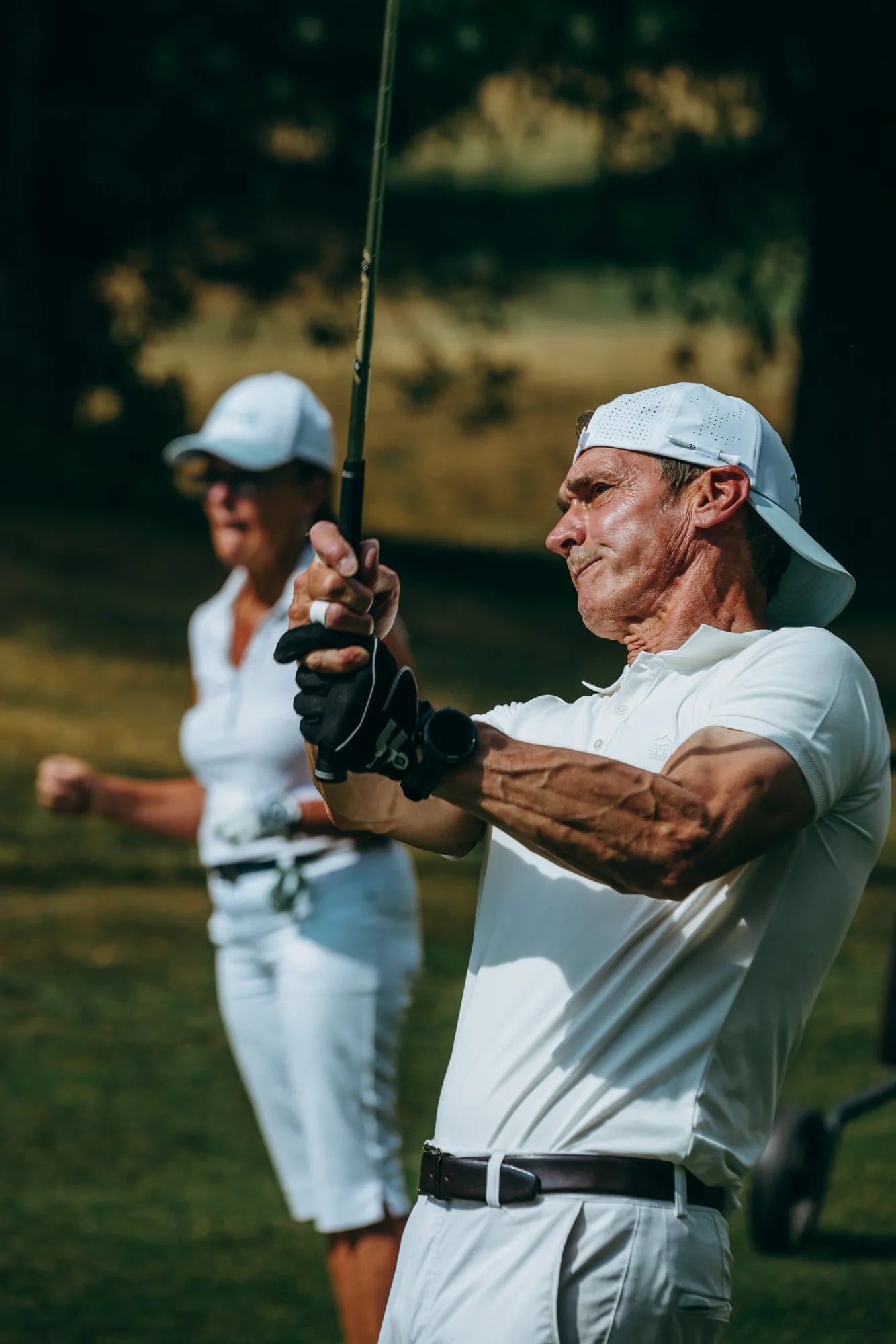 Golf ambassador in white KADI apparel mid-swing follow-through on the course