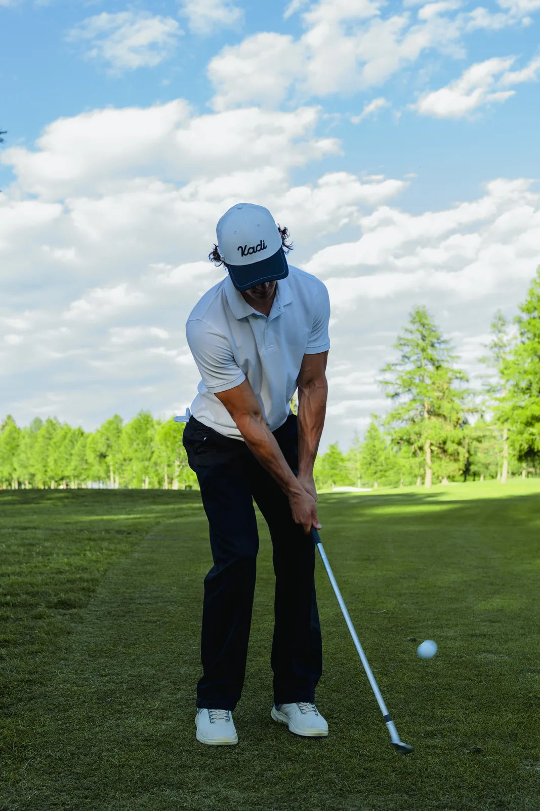Golfer in a white KADI cap at the moment of the swing