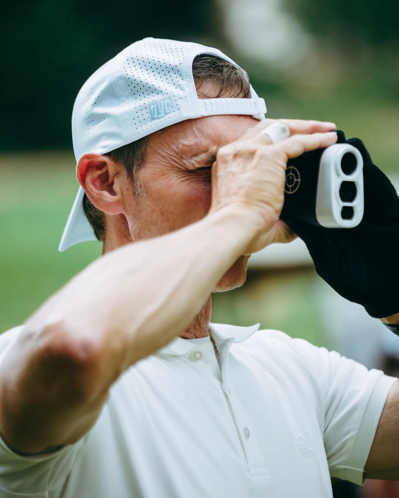 Golfer using a rangefinder wearing a white KADI cap on the course