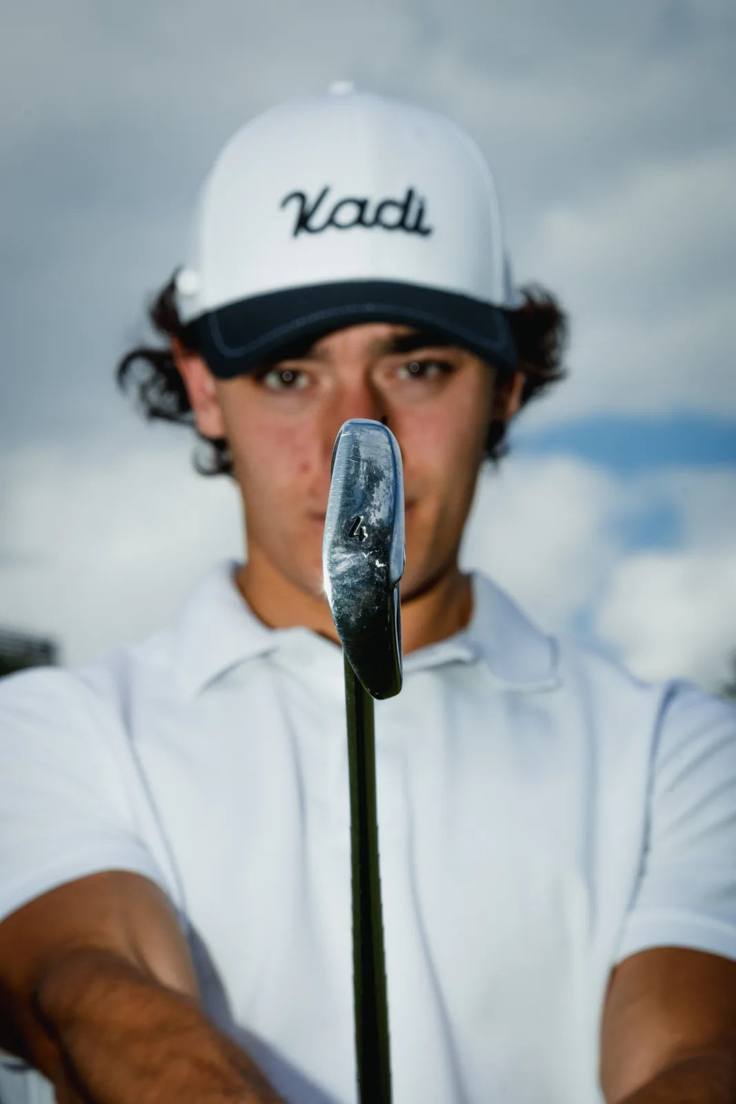 Man in a KADI cap holding a golf club upright on the course